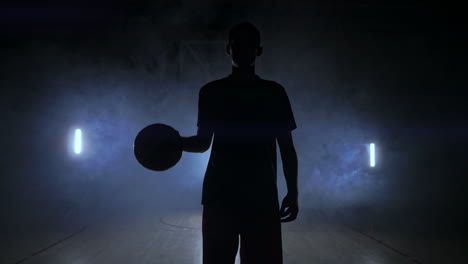 Männlicher-Basketballspieler,-Der-Sich-Im-Rauch-Vor-Der-Kamera-Bewegt-Und-Den-Ball-In-Zeitlupe-Mit-Steadicam-Aufnahme-über-Den-Parkettboden-Wirft